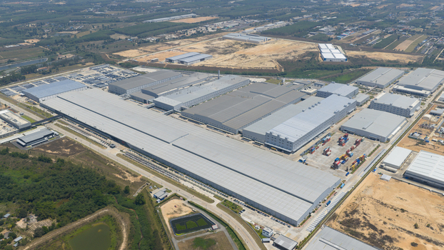 Aerial view of the BYD Auto Thailand factory complex with large industrial buildings grey rooftops and surrounding green fields in Phananikhom Rayong Thailand.