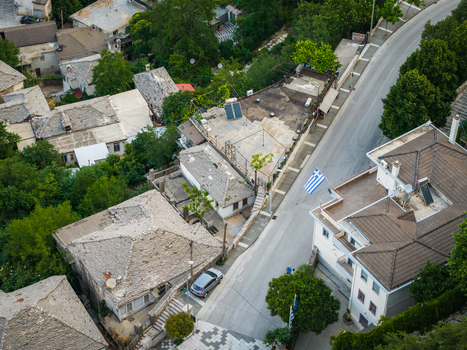 Aerial view of traditional stone rooftops and a narrow street with a Greek flag and lush green trees in Gjirokaster Gjirokaster County Albania. Aerial view of traditional stone rooftops and a narrow street with a Greek flag and lush green trees in Gjirokaster Gjirokaster County Albania.