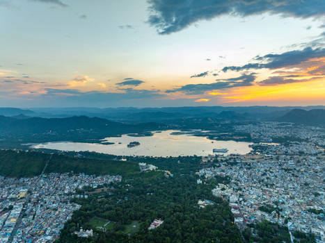 Aerial view of Lake Pichola at sunset with the city of Udaipur historic architecture and surrounding hills in Udaipur Rajasthan India.
