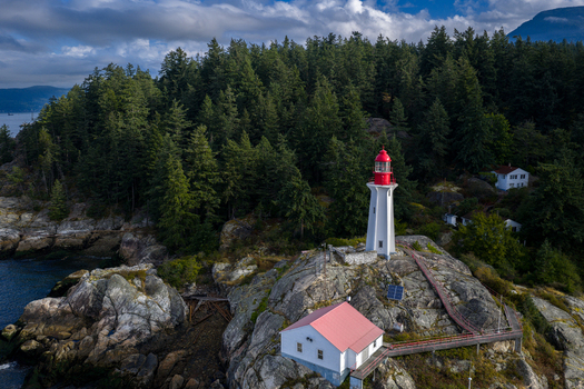 Aerial view of Point Atkinson Lighthouse surrounded by dense evergreen forest and rocky coastline in West Vancouver British Columbia Canada.