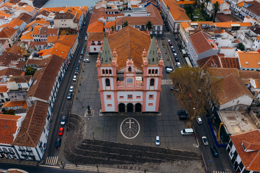 Aerial view of the Se Cathedral with its pink facade and twin towers overlooking a paved square and orange tiled rooftops in Angra do Heroismo Azores Portugal.