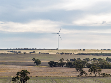 Aerial view of a wind turbine standing in a rural landscape with agricultural fields scattered trees and a cloudy sky in Kiata Victoria Australia. Aerial view of a wind turbine standing in a rural landscape with agricultural fields scattered trees and a cloudy sky in Kiata Victoria Australia.
