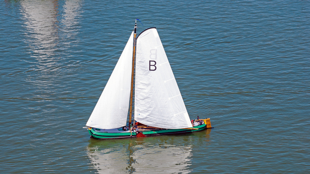 Aerial view of a traditional Dutch sailing boat with white sails navigating the calm waters of the IJsselmeer in Hindeloopen Friesland Netherlands. Aerial view of a traditional Dutch sailing boat with white sails navigating the calm waters of the IJsselmeer in Hindeloopen Friesland Netherlands.