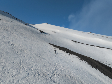 Aerial view of the south side of Mount Etna with a lone skier ascending the snowy volcanic slope under a clear blue sky in Nicolosi Sicilia Italy. Aerial view of the south side of Mount Etna with a lone skier ascending the snowy volcanic slope under a clear blue sky in Nicolosi Sicilia Italy.
