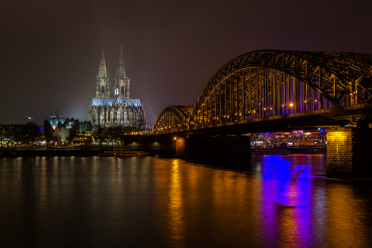 View of the illuminated Cologne Cathedral and Hohenzollern Bridge reflecting in the Rhine river at night Cologne North Rhine Westphalia Germany.
