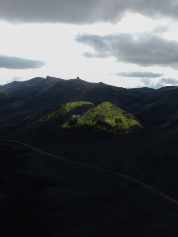 Aerial view of a small hill covered in vibrant green moss contrasts against the surrounding dark volcanic landscape Iceland. Aerial view of a small hill covered in vibrant green moss contrasts against the surrounding dark volcanic landscape Iceland.