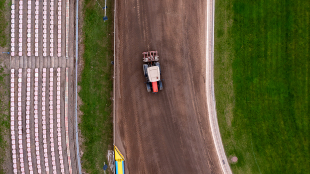 Aerial view of a tractor grooming the dirt surface of a speedway track next to stadium seating and green grass in Gdansk Poland.
