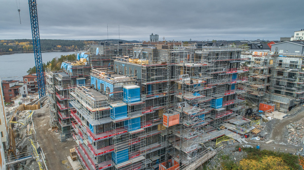 Aerial view of a large residential construction site featuring multi story buildings covered in scaffolding and blue protective sheeting with a tall crane nearby Sweden. Aerial view of a large residential construction site featuring multi story buildings covered in scaffolding and blue protective sheeting with a tall crane nearby Sweden.
