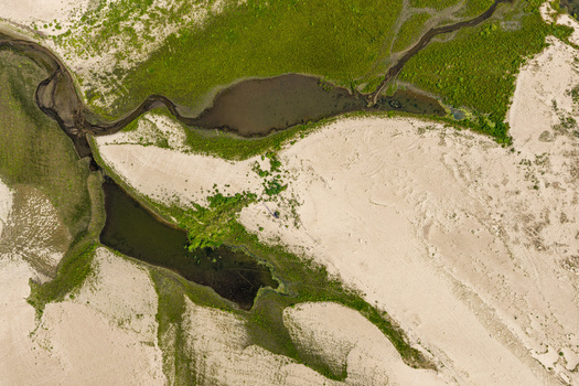 Aerial view of a riverbed with low water levels exposed sandbanks and patches of green vegetation in Poland.