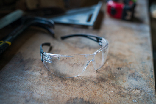 View of safety glasses resting on a worn wooden workbench with a hammer square and tape measure in the background in Looe Cornwall United Kingdom. View of safety glasses resting on a worn wooden workbench with a hammer square and tape measure in the background in Looe Cornwall United Kingdom.