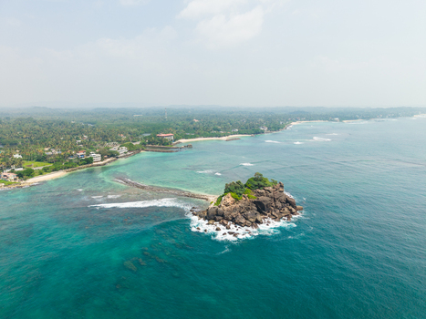 Aerial view of Devil s Rock surrounded by turquoise ocean waters and a lush tropical coastline Ahangama Southern Province Sri Lanka. Aerial view of Devil s Rock surrounded by turquoise ocean waters and a lush tropical coastline Ahangama Southern Province Sri Lanka.