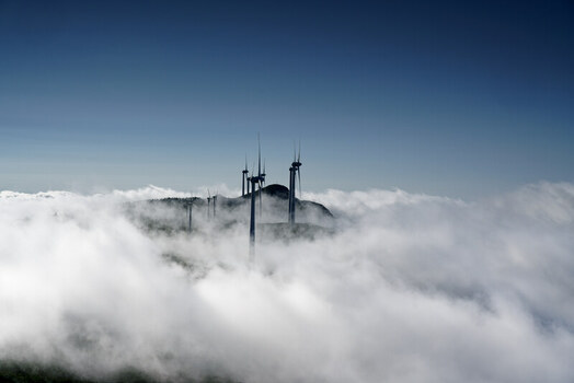 Aerial view of wind turbines on Bica da Cana peak rising above a dense sea of clouds under a clear blue sky in Funchal Madeira Portugal.