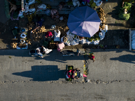 Aerial view of a street market with vendors produce sacks a blue umbrella and people on motorcycles in Kemalang Central Java Indonesia.