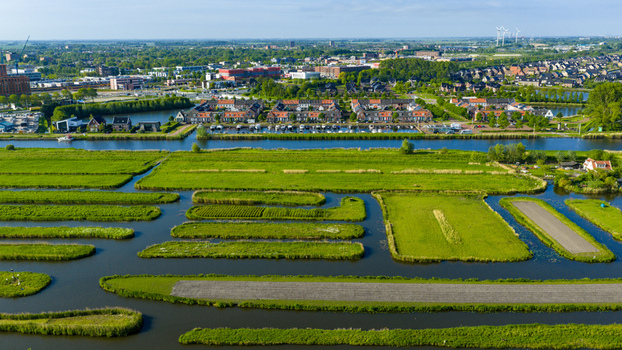 Aerial view of Oosterdel nature reserve featuring unique green islands and waterways with residential houses in the background Broek op Langedijk Noord Holland Netherlands. Aerial view of Oosterdel nature reserve featuring unique green islands and waterways with residential houses in the background Broek op Langedijk Noord Holland Netherlands.