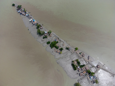 Aerial view of Kalabagi village on a narrow strip of land with small huts and green trees surrounded by murky river water in Khulna District Khulna Division Bangladesh.