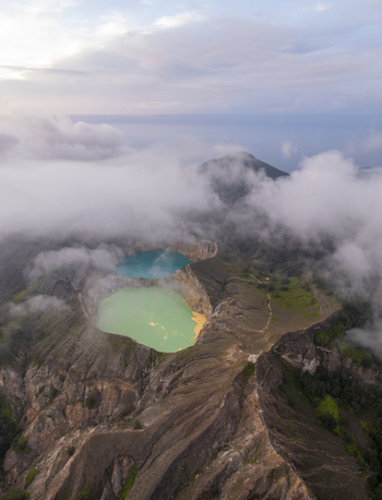 Aerial view of the volcanic crater lakes of Kelimutu National Park with turquoise and green water surrounded by rugged mountain terrain and mist in Detusoko East Nusa Tenggara Indonesia.