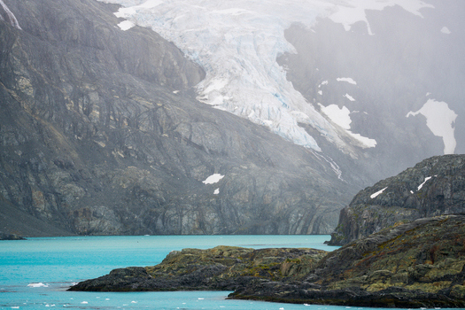 View of Drygalski Fjord featuring a massive glacier descending into turquoise waters surrounded by rugged rocky mountains in South Georgia and the South Sandwich Islands.