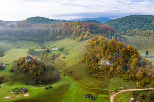 Aerial view of Fundatura Ponorului featuring rolling green hills autumn forests haystacks and rural houses in the Carpathian Mountains. Ohaba Ponor Hunedoara Romania.