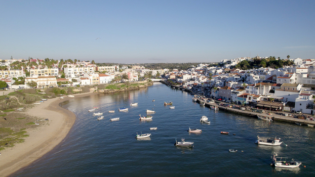 Aerial view of the coastal village of Ferragudo with white washed houses along the riverbank small fishing boats in the water and a sandy beach. Ferragudo Faro District Portugal.