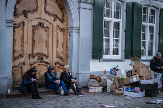 Basel Switzerland 10 March 2025 View of women seated on steps before a grand wooden door amidst scattered boxes and a backdrop of aged architecture. Basel Switzerland 10 March 2025 View of women seated on steps before a grand wooden door amidst scattered boxes and a backdrop of aged architecture.