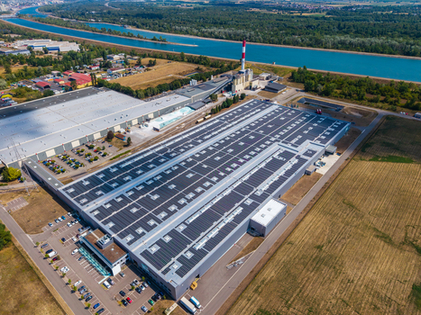 Aerial view of the Glas Trosch Alsace SAS industrial facility with solar panels on the roof parking lot and nearby canal in Hombourg Grand Est France.