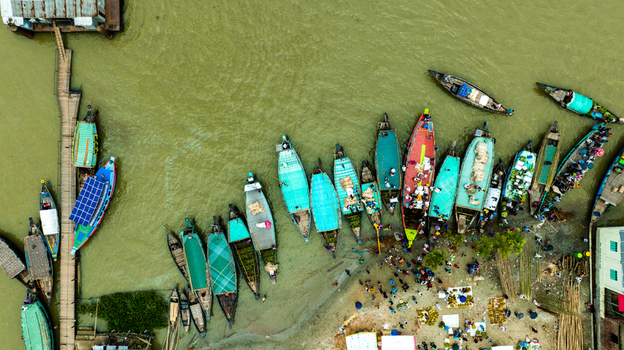 Aerial view of Baish Mowza Sarak Bazar with colorful wooden boats docked along the riverbank people on the shore and a wooden pier in Nabinagar Chittagong Division Bangladesh. Aerial view of Baish Mowza Sarak Bazar with colorful wooden boats docked along the riverbank people on the shore and a wooden pier in Nabinagar Chittagong Division Bangladesh.
