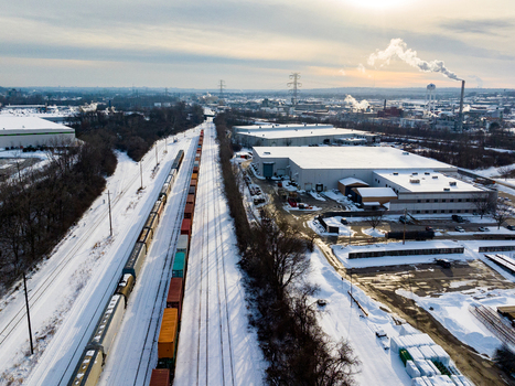 Aerial view of a freight train on snow covered tracks passing through an industrial area with warehouses and rising steam under a winter sky Reading Ohio United States. Aerial view of a freight train on snow covered tracks passing through an industrial area with warehouses and rising steam under a winter sky Reading Ohio United States.