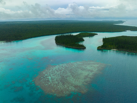 Aerial view of turquoise waters embrace the land revealing coral reefs and dense forests under a cloudy sky Pine Island L Île des Pins New Caledonia. Aerial view of turquoise waters embrace the land revealing coral reefs and dense forests under a cloudy sky Pine Island L Île des Pins New Caledonia.