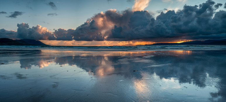 View of dramatic sunset clouds reflecting on the wet sand of the shoreline with distant mountains Inch Beach County Kerry Ireland. View of dramatic sunset clouds reflecting on the wet sand of the shoreline with distant mountains Inch Beach County Kerry Ireland.