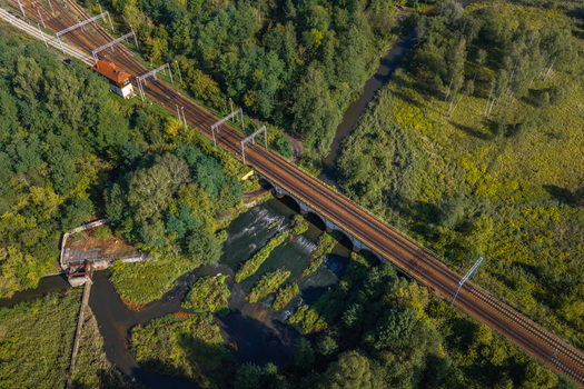 Aerial view of a railway bridge crossing a river surrounded by lush green trees and vegetation in Sosnowiec Silesian Voivodeship Poland. Aerial view of a railway bridge crossing a river surrounded by lush green trees and vegetation in Sosnowiec Silesian Voivodeship Poland.