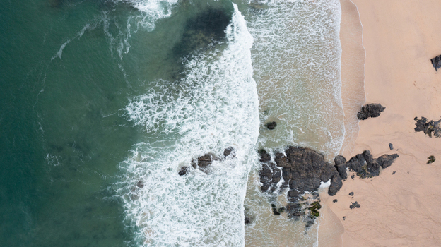 Aerial view of Harlyn Bay Beach with turquoise waves crashing against dark rocks and golden sand in Saint Merryn Cornwall United Kingdom.