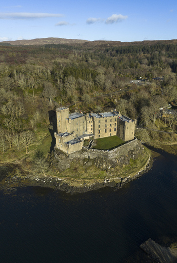 Aerial view of Dunvegan Castle and Gardens a historic stone fortress on a rocky cliff overlooking the sea surrounded by dense woodland in Isle of Skye Scotland United Kingdom. Aerial view of Dunvegan Castle and Gardens a historic stone fortress on a rocky cliff overlooking the sea surrounded by dense woodland in Isle of Skye Scotland United Kingdom.