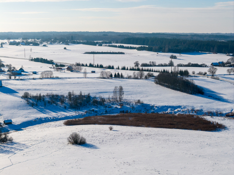 Aerial view of snow covered rural landscape with scattered farmsteads dense pine forests and rolling white fields under a clear winter sky in Lithuania. Aerial view of snow covered rural landscape with scattered farmsteads dense pine forests and rolling white fields under a clear winter sky in Lithuania.