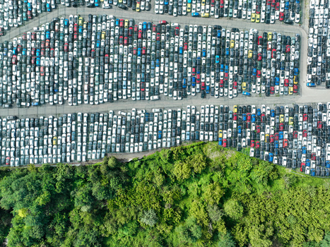 Aerial view of a large car storage facility with rows of colorful vehicles parked next to a lush green forest in Turin Piedmont Italy.