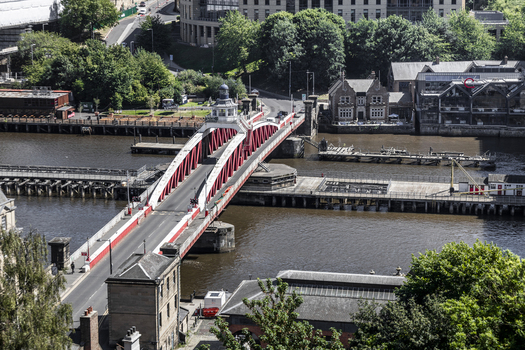 Aerial view of the historic Swing Bridge crossing the River Tyne surrounded by urban architecture stone buildings and lush green trees in Newcastle upon Tyne England United Kingdom. Aerial view of the historic Swing Bridge crossing the River Tyne surrounded by urban architecture stone buildings and lush green trees in Newcastle upon Tyne England United Kingdom.