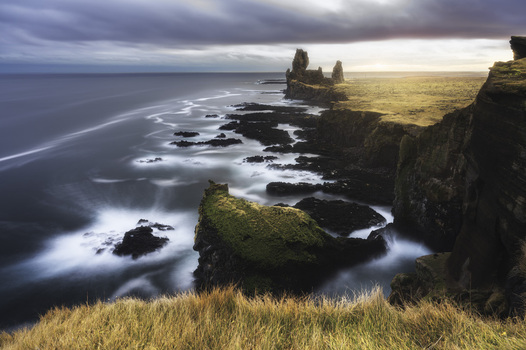 View of Londrangar basalt cliffs and the dramatic coastline with crashing waves under a cloudy sky at sunset in Hellnar Snaefellsbaer Iceland.