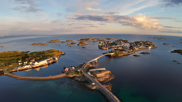 Aerial view of Lofoten islands featuring a bridge connecting coastal settlements surrounded by deep blue sea and rocky islets under a sunset sky in Vagan Municipality Nordland Norway. Aerial view of Lofoten islands featuring a bridge connecting coastal settlements surrounded by deep blue sea and rocky islets under a sunset sky in Vagan Municipality Nordland Norway.