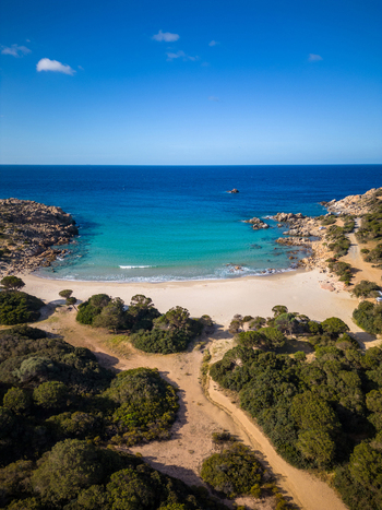 Aerial view of Spiaggia di Cala Cipolla with turquoise waters white sandy beach and rugged rocky cliffs under a clear blue sky in Chia Sardegna Italy.