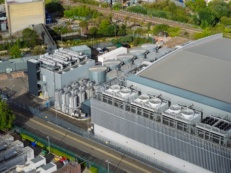 Aerial view of a data center facility featuring industrial cooling units ventilation systems and technical infrastructure surrounded by greenery and a railway line in the United Kingdom. Aerial view of a data center facility featuring industrial cooling units ventilation systems and technical infrastructure surrounded by greenery and a railway line in the United Kingdom.