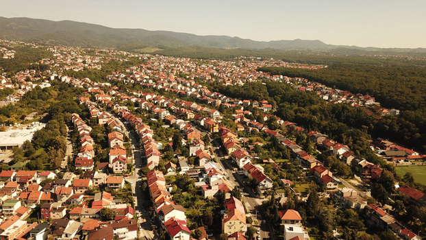 Aerial view of a residential neighborhood with red roofed houses surrounded by lush green trees and hills in Zagreb Croatia.