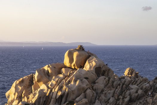 View of the unique granite rock formations of Capo Testa with people standing on the peaks overlooking the blue Mediterranean sea during sunset Capo Testa Sardegna Italy. View of the unique granite rock formations of Capo Testa with people standing on the peaks overlooking the blue Mediterranean sea during sunset Capo Testa Sardegna Italy.
