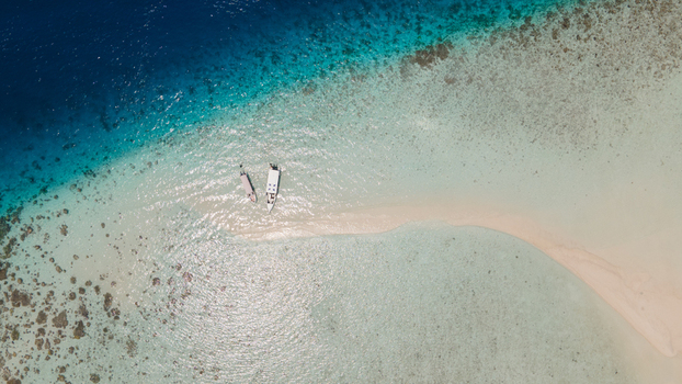 Aerial view of a white sandbar surrounded by shallow turquoise water and coral reefs with two boats anchored in Raja Ampat Southwest Papua Indonesia. Aerial view of a white sandbar surrounded by shallow turquoise water and coral reefs with two boats anchored in Raja Ampat Southwest Papua Indonesia.