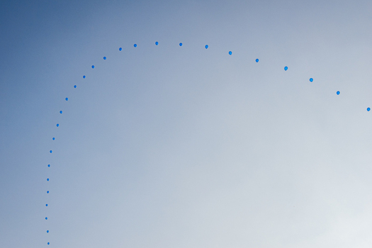 View of a series of small blue balloons floating in an arc across a clear blue sky in Switzerland.
