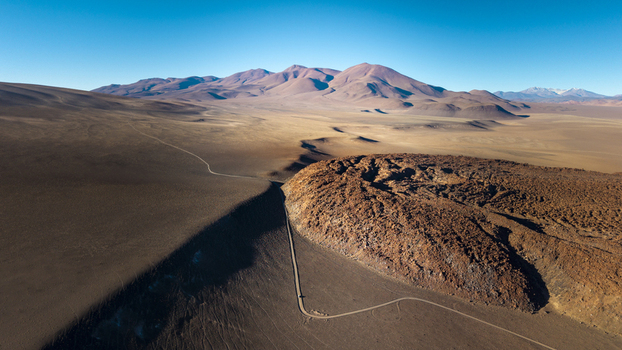 Aerial view of the arid volcanic landscape near Tolar Grande with a winding dirt road cutting through desert terrain and distant mountains in Tolar Grande Salta Province Argentina. Aerial view of the arid volcanic landscape near Tolar Grande with a winding dirt road cutting through desert terrain and distant mountains in Tolar Grande Salta Province Argentina.