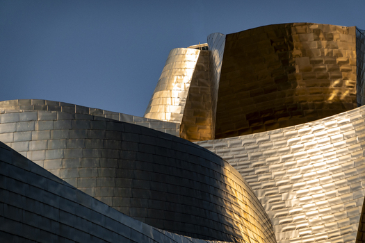 View of the Guggenheim Museum Bilbao featuring its iconic curved titanium panels reflecting golden sunlight against a clear blue sky Bilbao Euskadi Spain. View of the Guggenheim Museum Bilbao featuring its iconic curved titanium panels reflecting golden sunlight against a clear blue sky Bilbao Euskadi Spain.