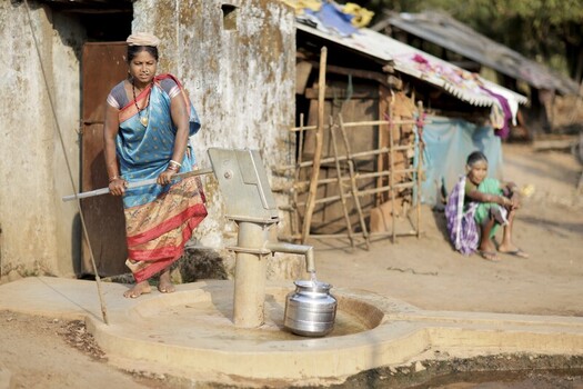 Odisha India 26 March 2026 View of a woman in a vibrant blue sari drawing water from a hand pump its silver spout gleaming against the rustic backdrop of a weathered hut. Odisha India 26 March 2026 View of a woman in a vibrant blue sari drawing water from a hand pump its silver spout gleaming against the rustic backdrop of a weathered hut.