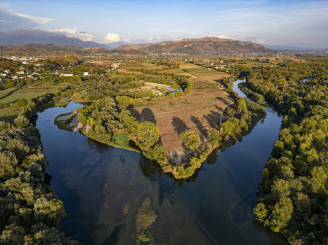 Aerial view of the Drin river winding through lush greenery and agricultural fields with mountains in the background in Shkoder Shkoder County Albania.