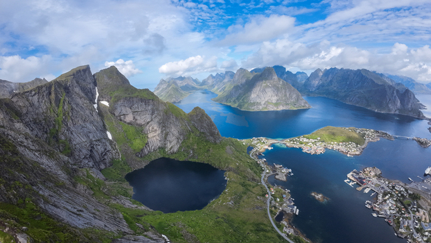 Aerial view of Lofoten islands featuring dramatic jagged mountains a deep blue lake coastal village and surrounding fjords in Vagan Municipality Nordland Norway. Aerial view of Lofoten islands featuring dramatic jagged mountains a deep blue lake coastal village and surrounding fjords in Vagan Municipality Nordland Norway.
