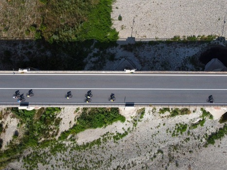 Aerial view of Ponte Crescentino with a group of cyclists crossing the bridge showing long shadows on the road above a dry riverbed in Verrua Savoia Piemonte Italy.