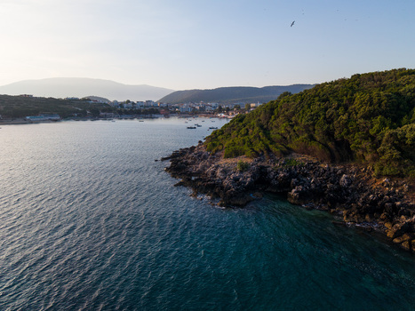 Aerial view of the turquoise sea and rocky coastline with lush green hills and the coastal town in the distance Ksamil Vlore County Albania. Aerial view of the turquoise sea and rocky coastline with lush green hills and the coastal town in the distance Ksamil Vlore County Albania.